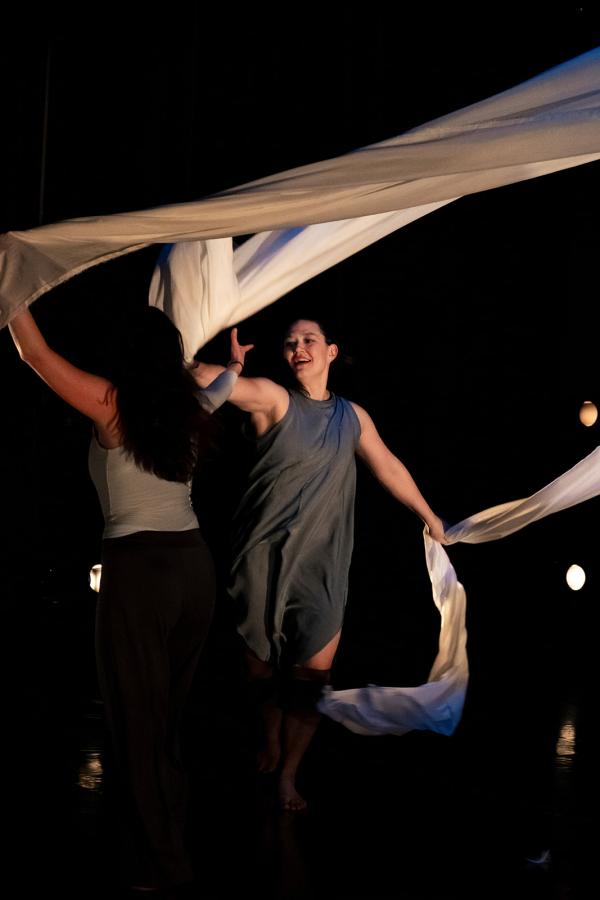 Two woman dance with large pieces of white fabric that look like large sails.  