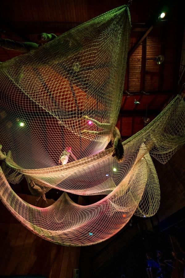 Four people are spread out in large layers of white netting suspended from the ceiling. Some of them dangle legs, arms or torsos from the edges.