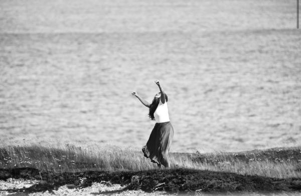 A woman dances on a cliff by the ocean.