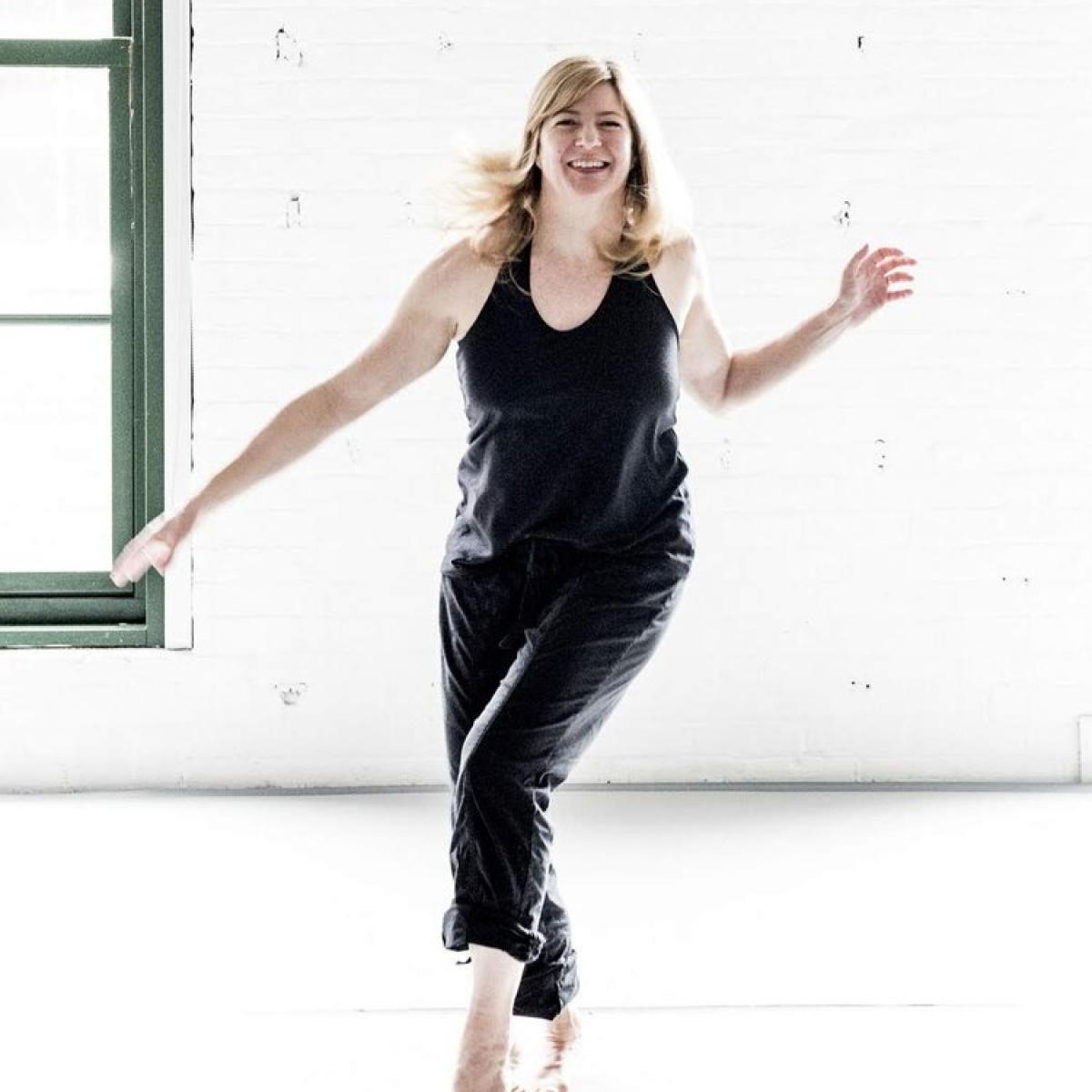 A woman in a black jumpsuit laughs and dances.