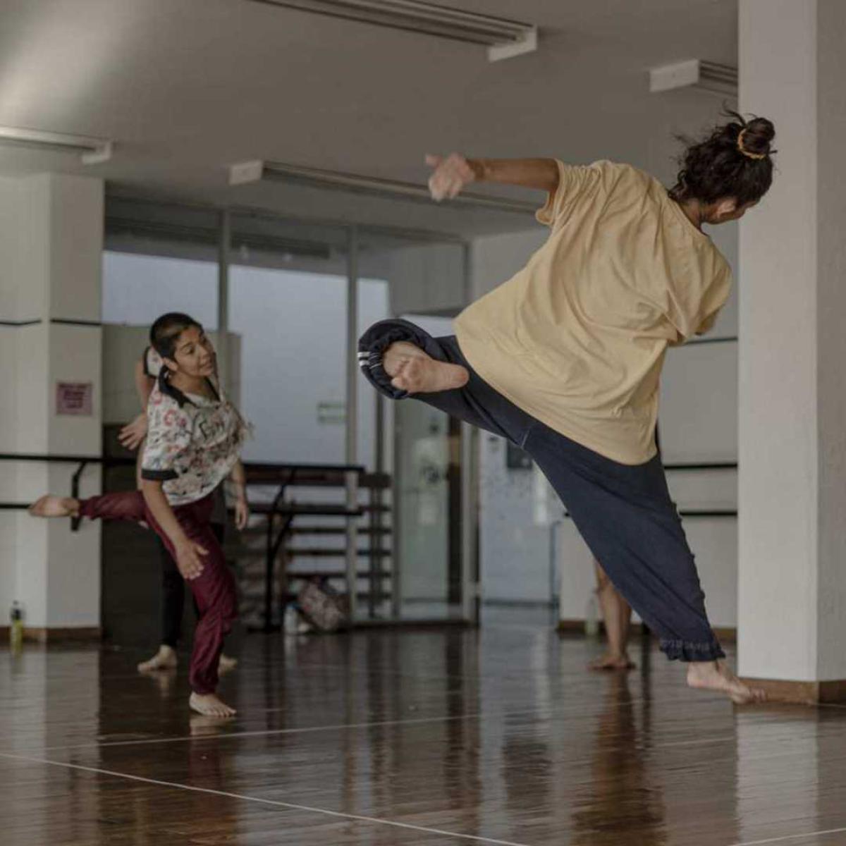 Two people dance in a studio, one jumping high, the other just landing.