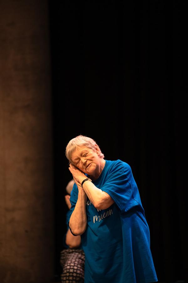 A caucasian elderly lady rests her head with her eyes closed on her hands in a sleep gesture against a black background