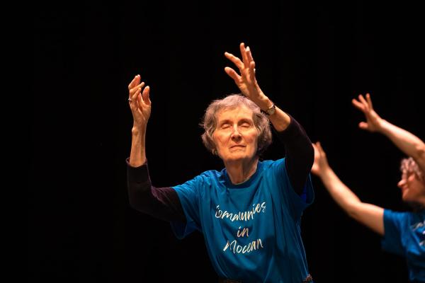 An elderly woman dances with her eyes closed